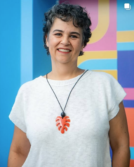 Julia com blusa branca e colar com fundo multicolorido